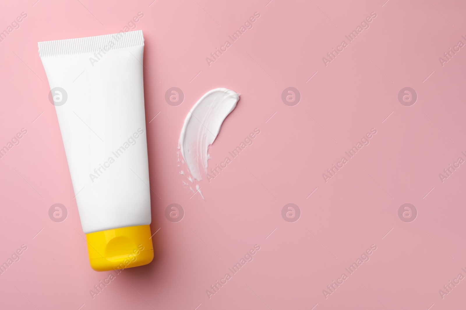 Photo of Tube of face cream and sample on pink background, top view. Space for text