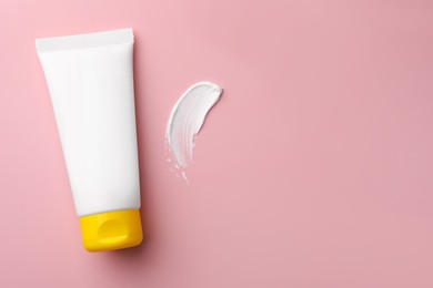 Photo of Tube of face cream and sample on pink background, top view. Space for text