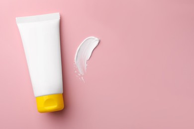 Tube of face cream and sample on pink background, top view. Space for text