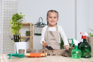 Little girl adding soil into peat pots at wooden table indoors. Growing vegetable seeds