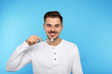 Young man brushing teeth on color background