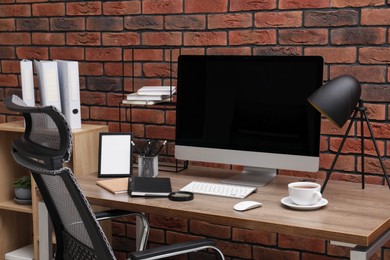 Photo of Cosy workspace with computer on desk, chair and bookcase near brick wall at home