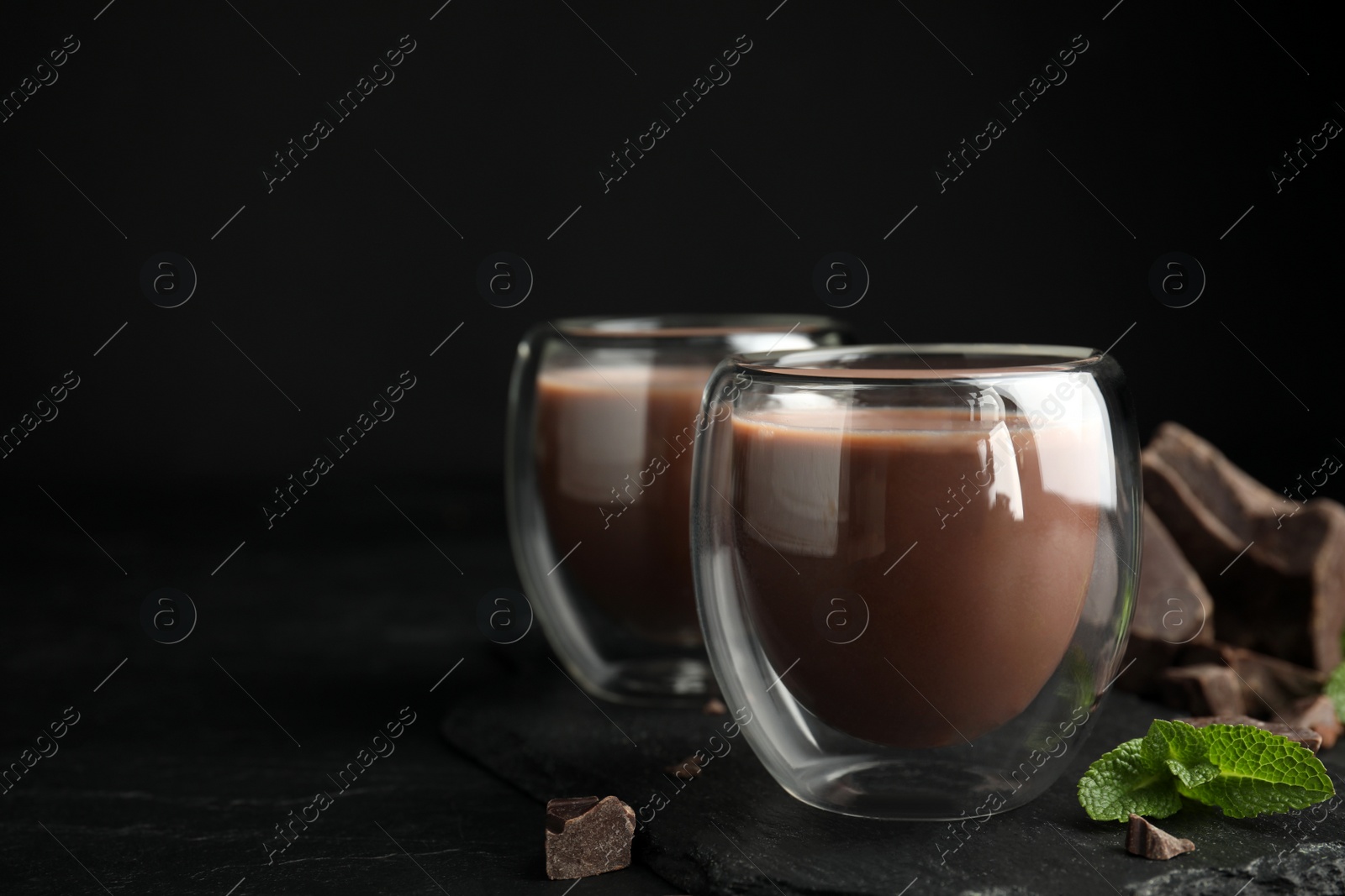 Photo of Glasses of delicious hot chocolate, chunks and fresh mint on black table. Space for text