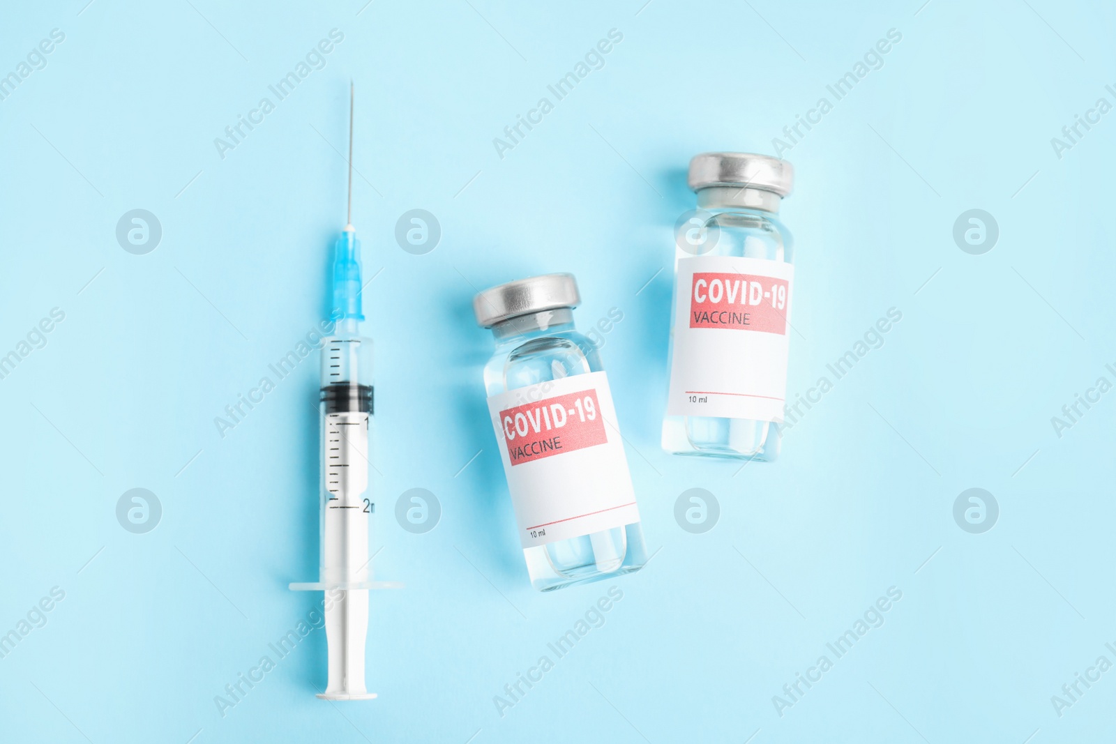 Photo of Vials with coronavirus vaccine and syringe on light blue background, flat lay