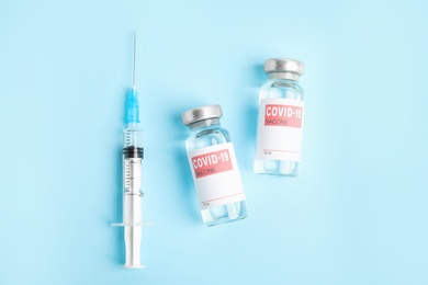 Photo of Vials with coronavirus vaccine and syringe on light blue background, flat lay