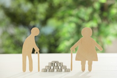 Pension savings. Figures of senior couple and coins on white table against blurred green background