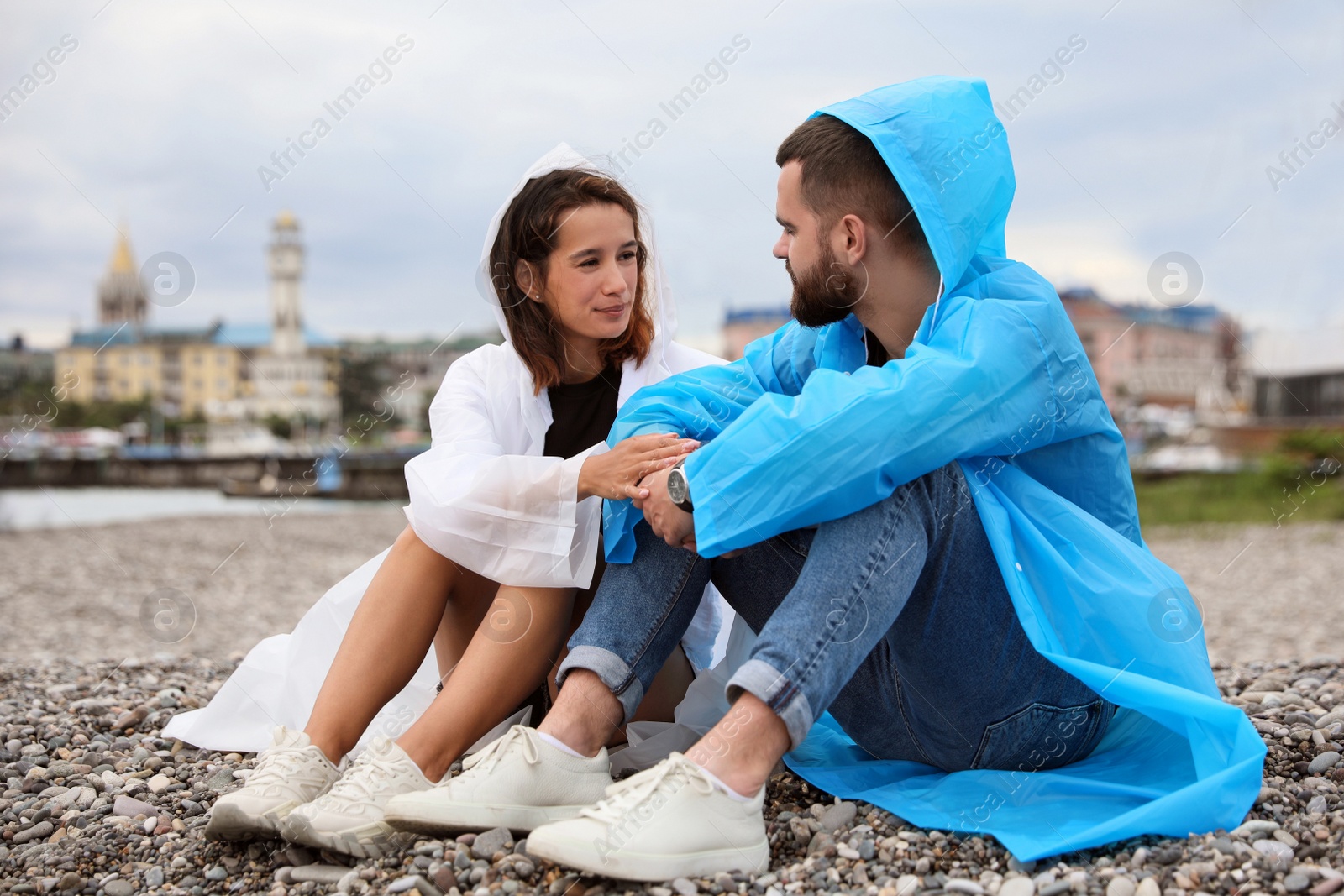 Photo of Young couple in raincoats enjoying time together under rain on beach