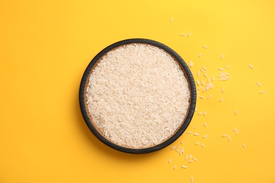 Plate with uncooked rice on color background, top view