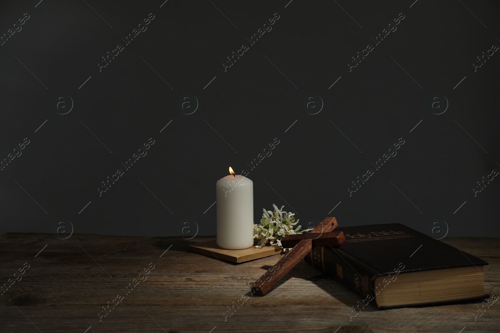 Photo of Church candle, flowers, cross and Bible on wooden table, space for text