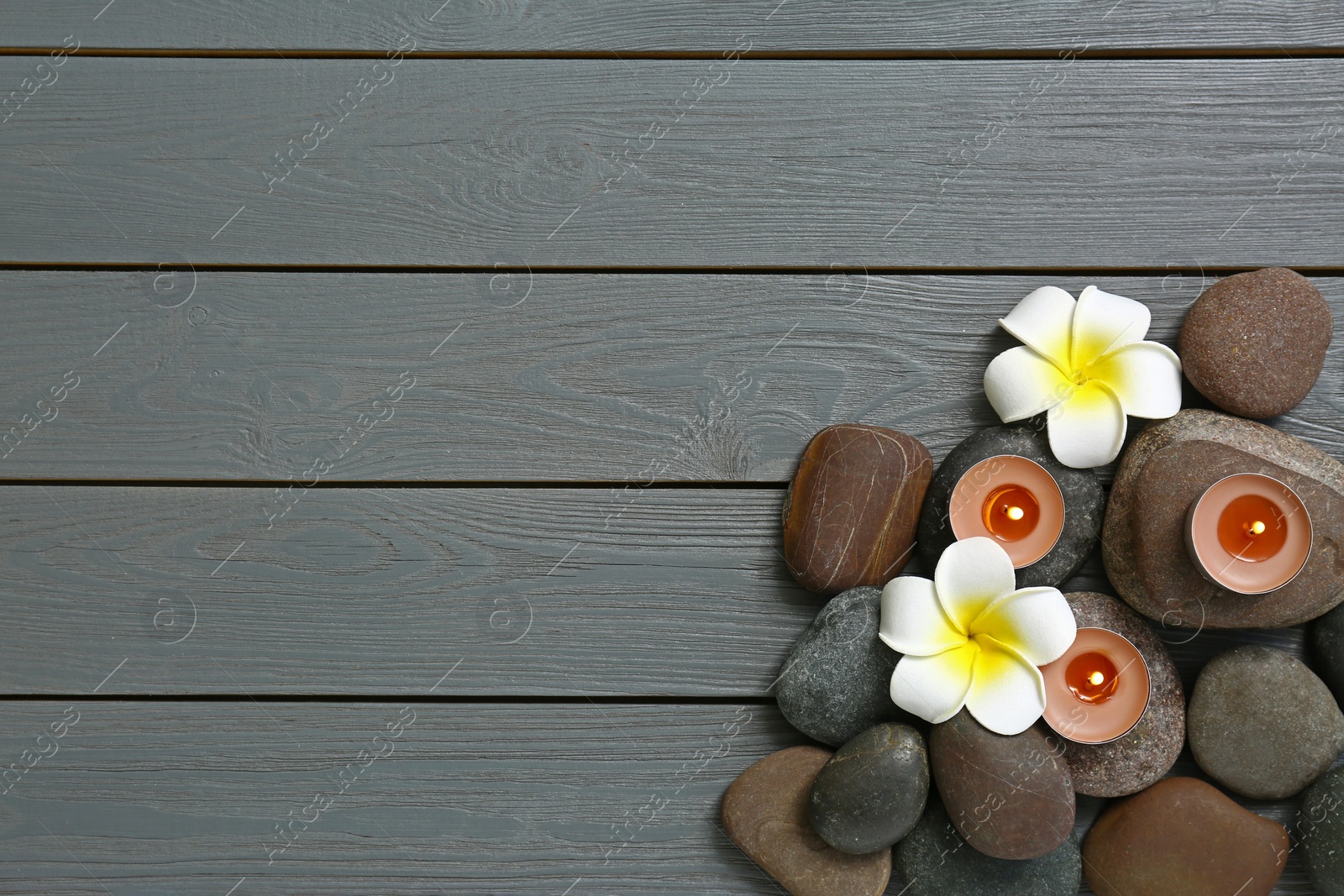 Photo of Flat lay composition with spa stones and flowers on grey wooden background, space for text