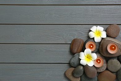 Flat lay composition with spa stones and flowers on grey wooden background, space for text