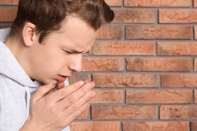 Photo of Teenage boy suffering from cough near brick wall. Space for text