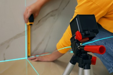 Photo of Woman using cross line laser level and tape for accurate measurement on tiled wall, closeup