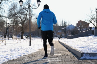 Photo of Man running along park on winter day, back view. Outdoors sports exercises