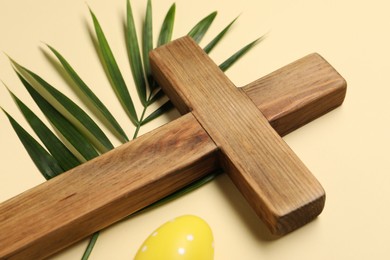 Wooden cross, painted Easter egg and palm leaf on beige background, closeup