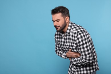 Photo of Unhappy man suffering from stomach pain on light blue background, space for text