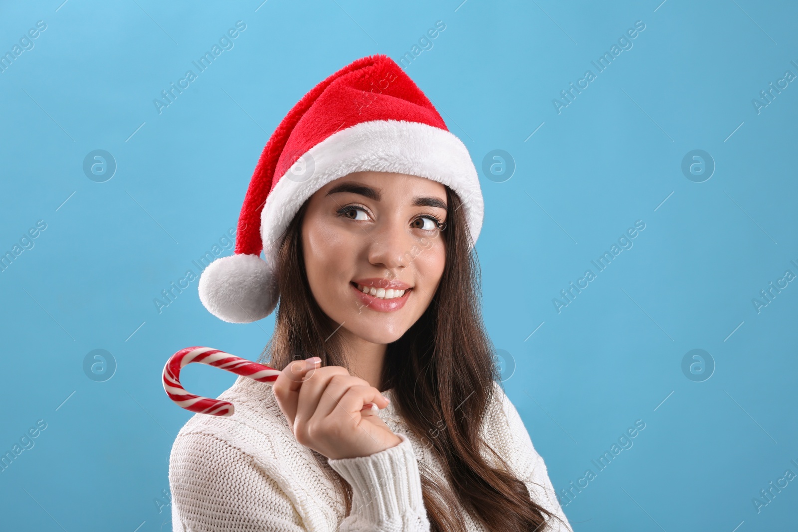 Photo of Beautiful woman in Santa Claus hat holding candy cane on light blue background