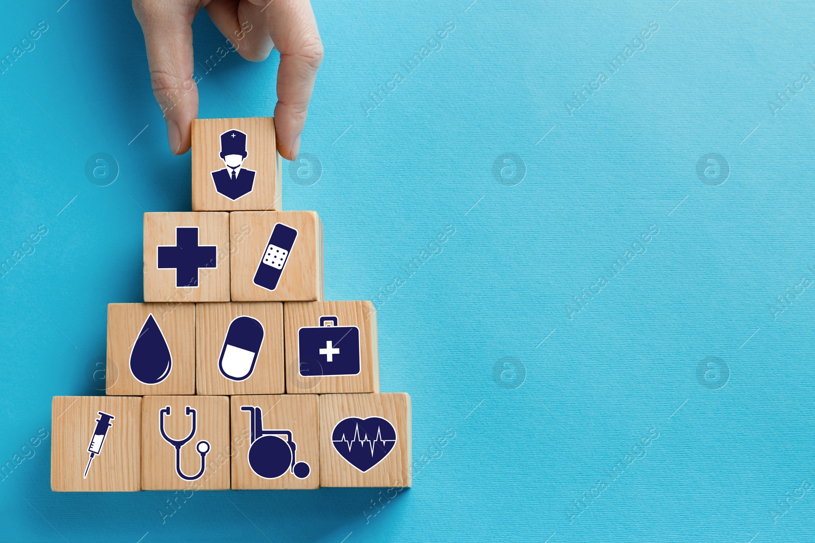 Image of Woman building pyramid of wooden cubes with different icons on turquoise background, top view. Insurance concept