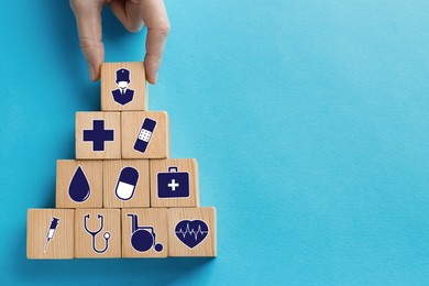 Image of Woman building pyramid of wooden cubes with different icons on turquoise background, top view. Insurance concept