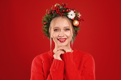 Beautiful young woman wearing Christmas wreath on red background