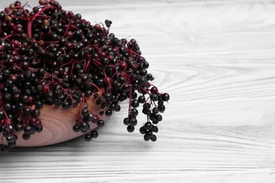 Photo of Tasty elderberries (Sambucus) on light blue wooden table, closeup. Space for text