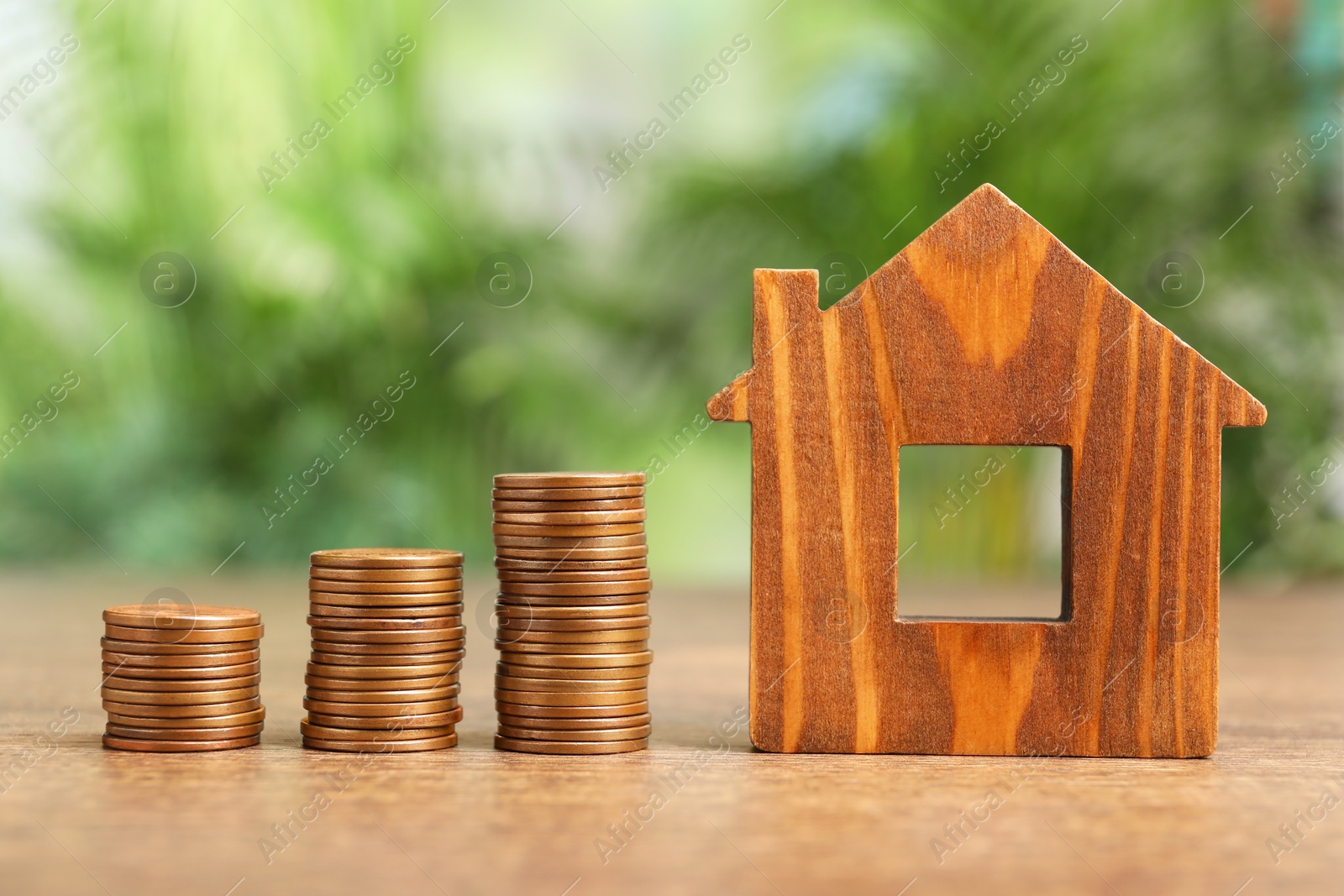 Photo of Mortgage concept. House model and stacks of coins on wooden table against blurred green background