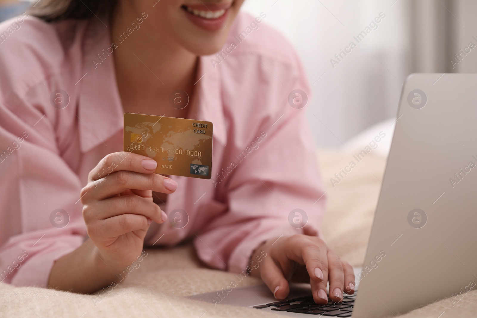 Photo of Woman with credit card using laptop for online shopping on bed indoors, closeup