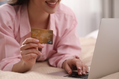 Photo of Woman with credit card using laptop for online shopping on bed indoors, closeup