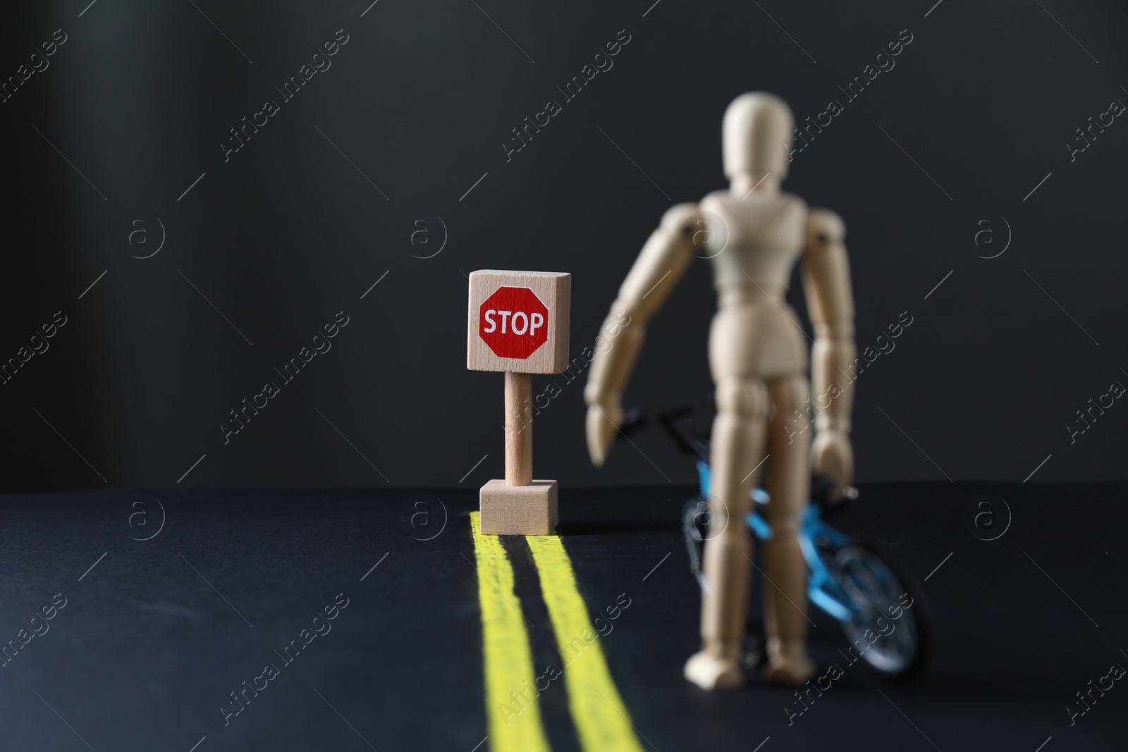 Photo of Development through barriers overcoming. Road Stop sign blocking way for wooden human figure with toy bicycle, space for text