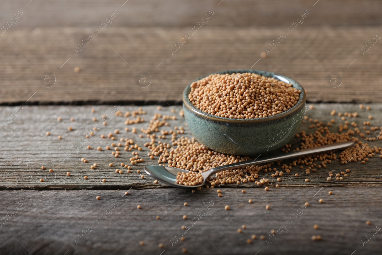 Photo of Bowl and spoon of mustard seeds on wooden table. Space for text