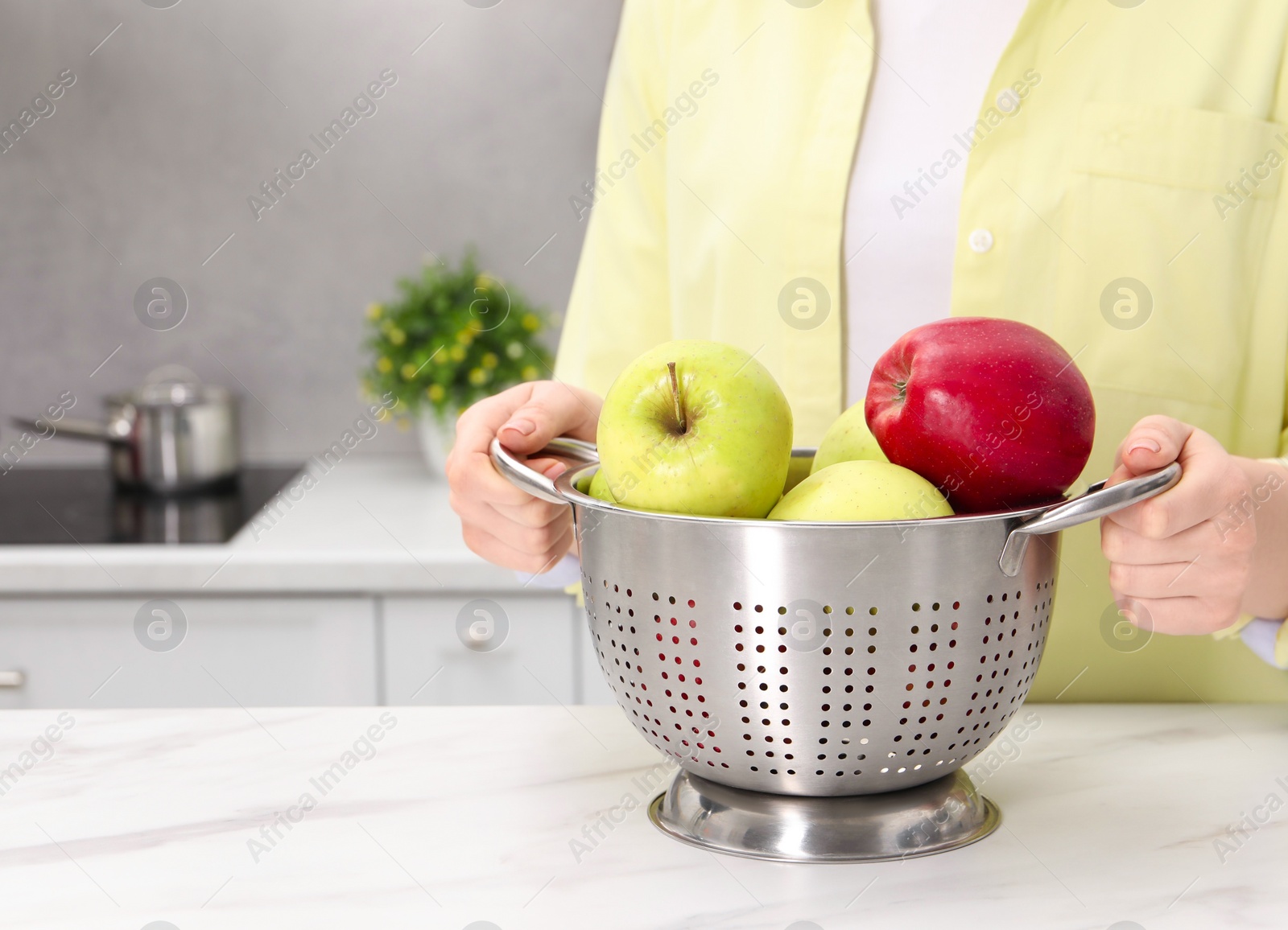 Photo of Woman holding colander with fresh apples at white marble table in kitchen, closeup. Space for text