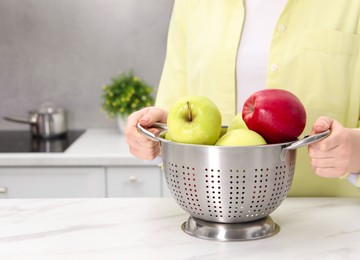 Photo of Woman holding colander with fresh apples at white marble table in kitchen, closeup. Space for text