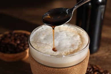 Photo of Pouring syrup into glass of tasty coffee on table, closeup