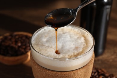 Pouring syrup into glass of tasty coffee on table, closeup