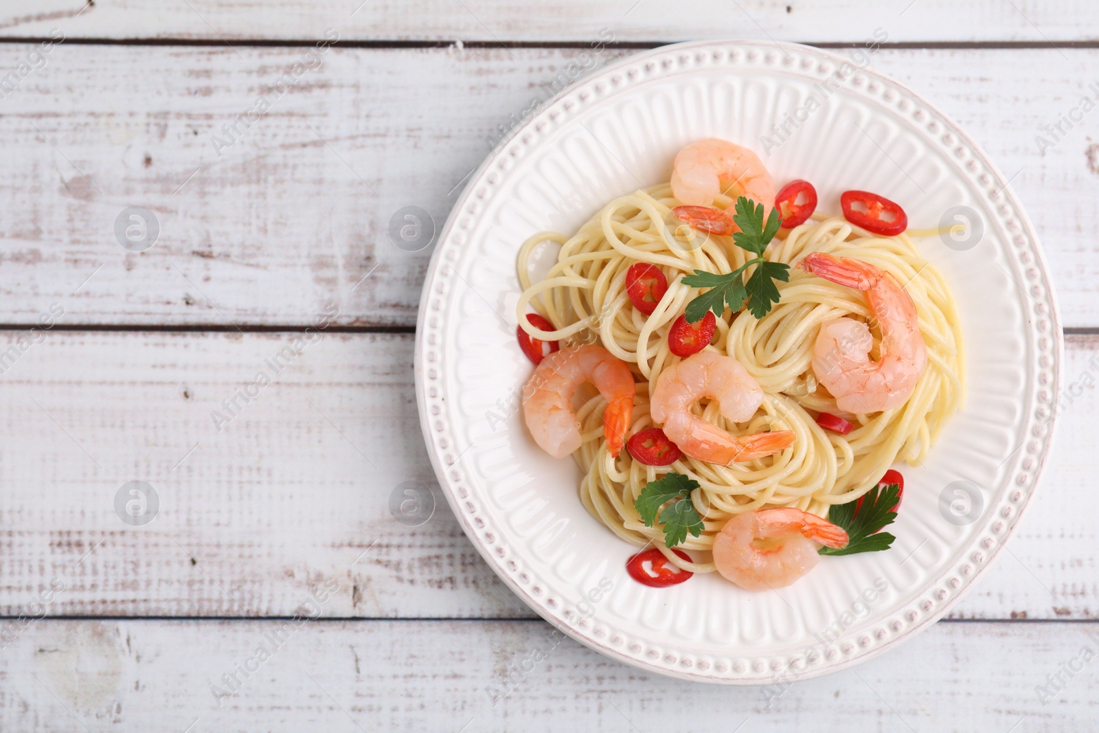 Photo of Tasty spaghetti with shrimps, chili pepper and parsley on wooden rustic table, top view. Space for text