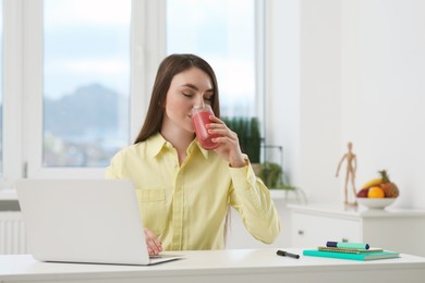 Photo of Beautiful young woman drinking delicious smoothie at workplace in office
