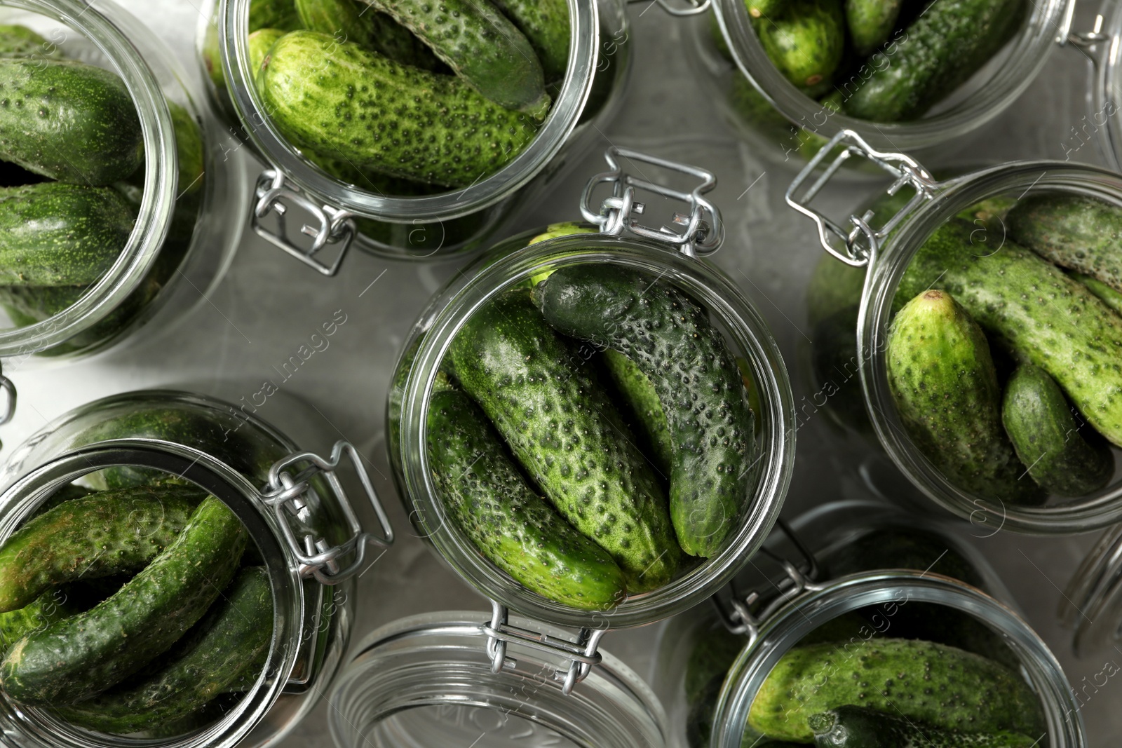 Photo of Pickling jars with fresh cucumbers on grey table, flat lay