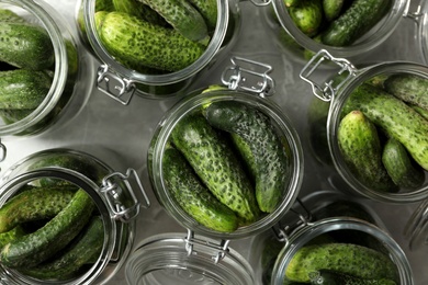Pickling jars with fresh cucumbers on grey table, flat lay