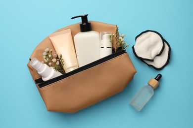 Photo of Preparation for spa. Compact toiletry bag with different cosmetic products and flowers on light blue background, flat lay