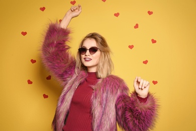 Photo of Beautiful young woman in fur coat with sunglasses posing on color background