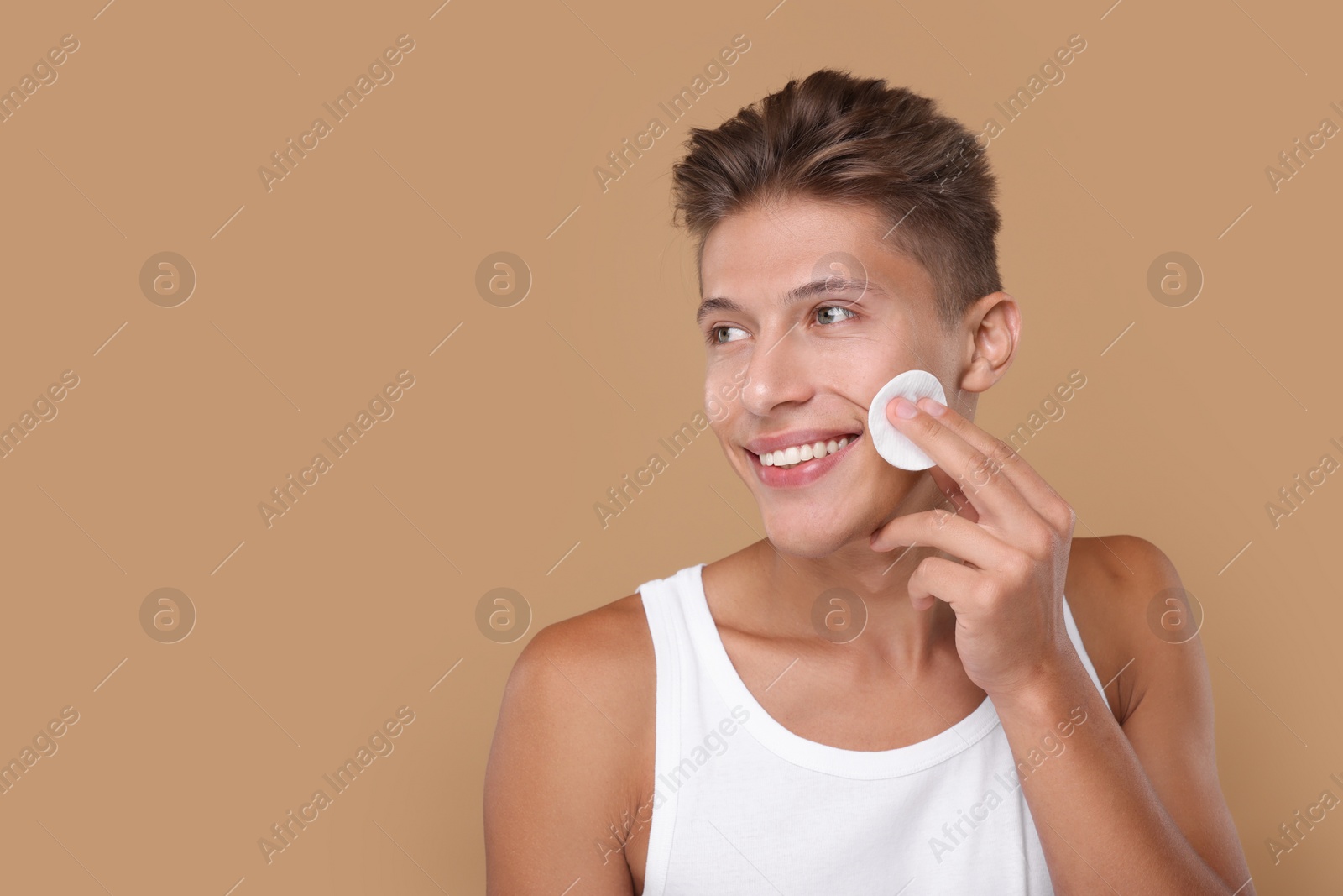Photo of Handsome man cleaning face with cotton pad on beige background, space for text