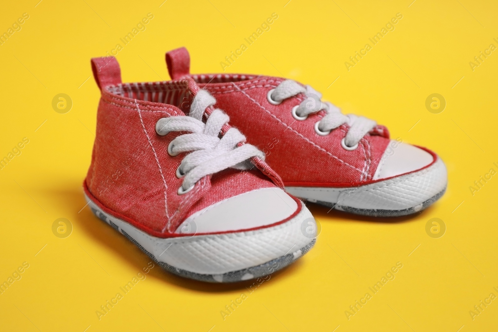 Photo of Pair of cute baby shoes on yellow background, closeup