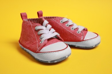 Pair of cute baby shoes on yellow background, closeup