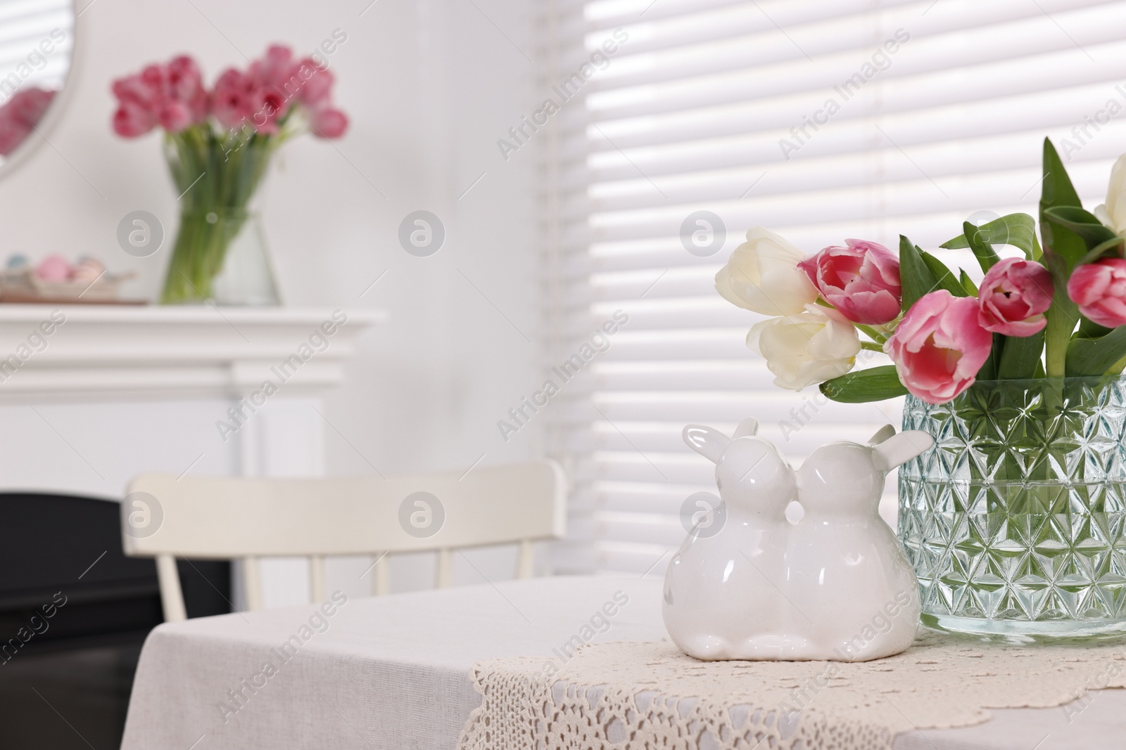 Photo of Easter decorations. Bouquet of tulips in vase and bunny figures on white table at home