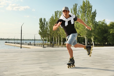 Handsome young man roller skating on pier near river, space for text