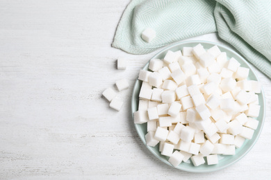 Photo of Refined sugar cubes on white wooden table, flat lay. Space for text