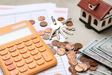 Photo of House model with calculator, documents, keys and money on table, closeup. Real estate agent service
