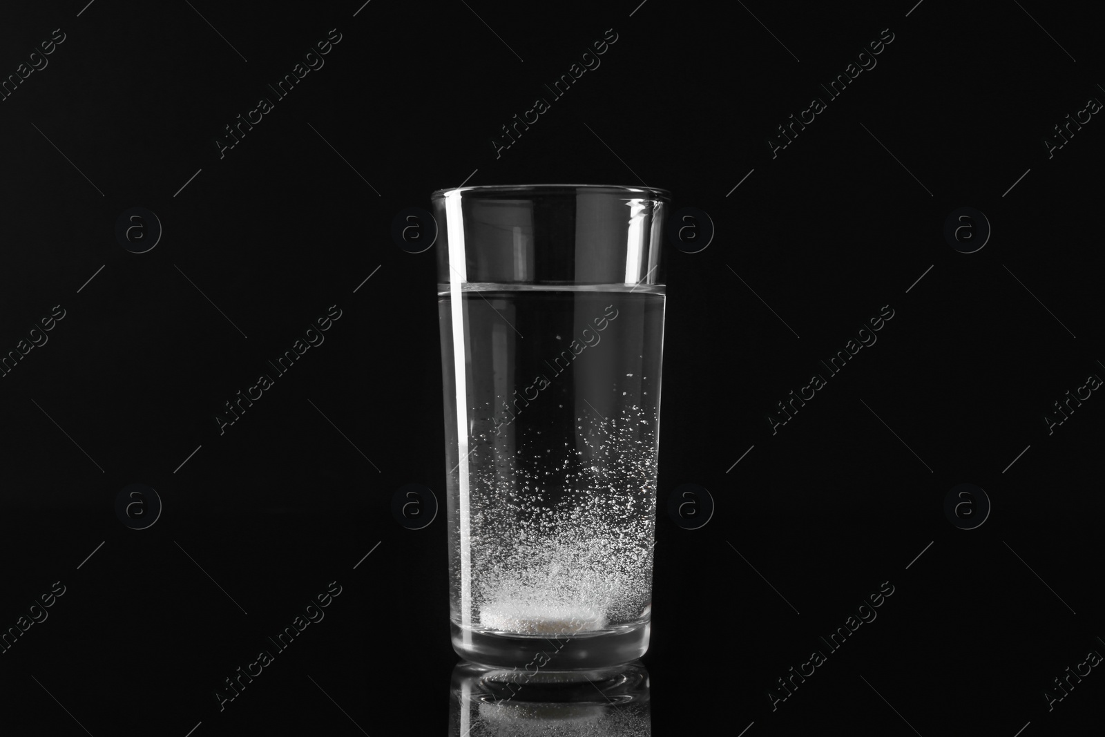 Photo of Effervescent pill dissolving in glass of water on black background