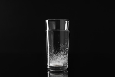 Photo of Effervescent pill dissolving in glass of water on black background