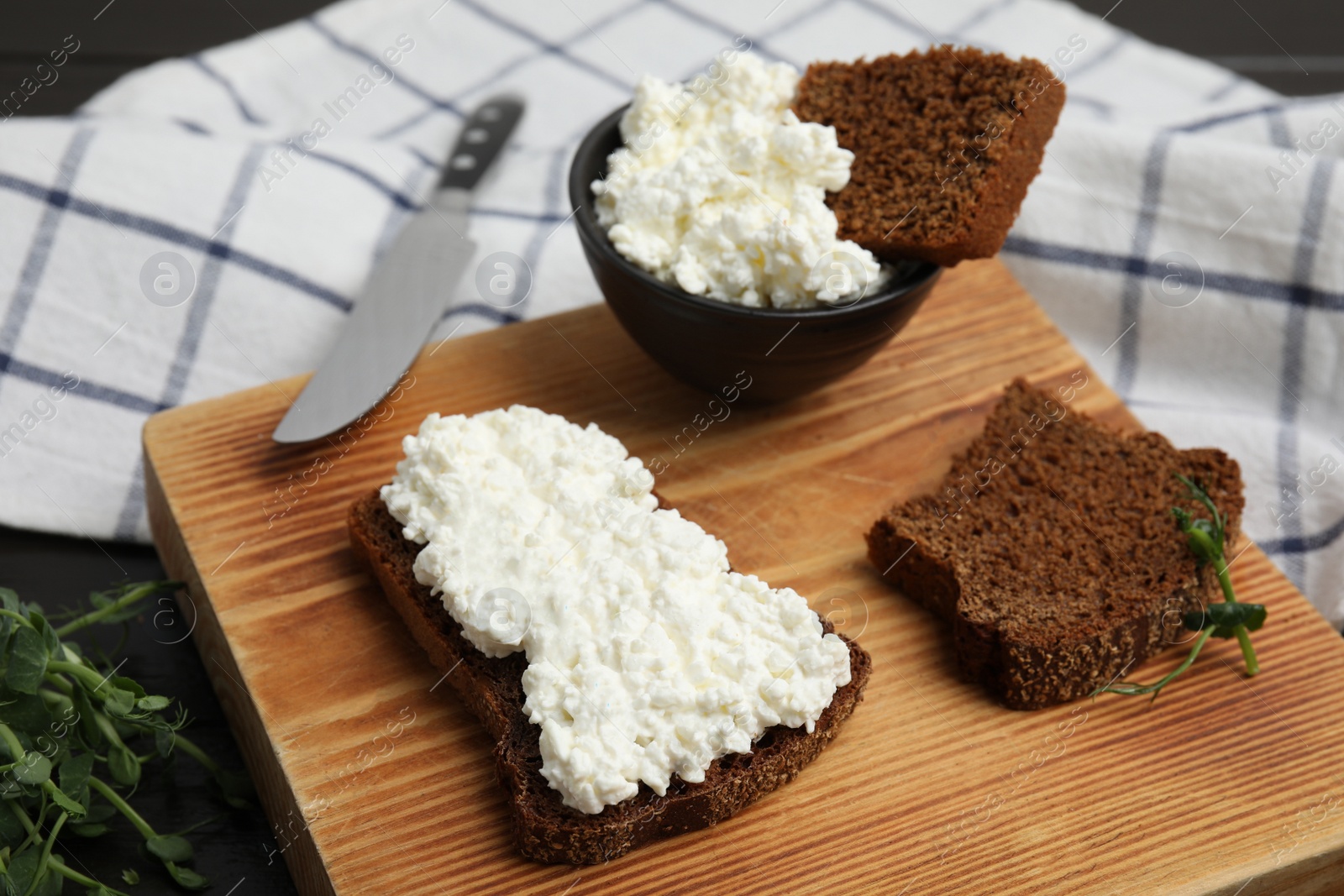 Photo of Bread with cottage cheese and microgreens on wooden board, closeup